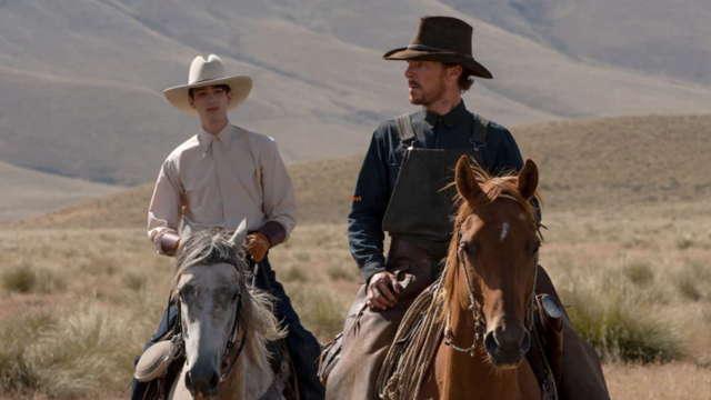 Two men wearing cowboy hats riding two horses in a field